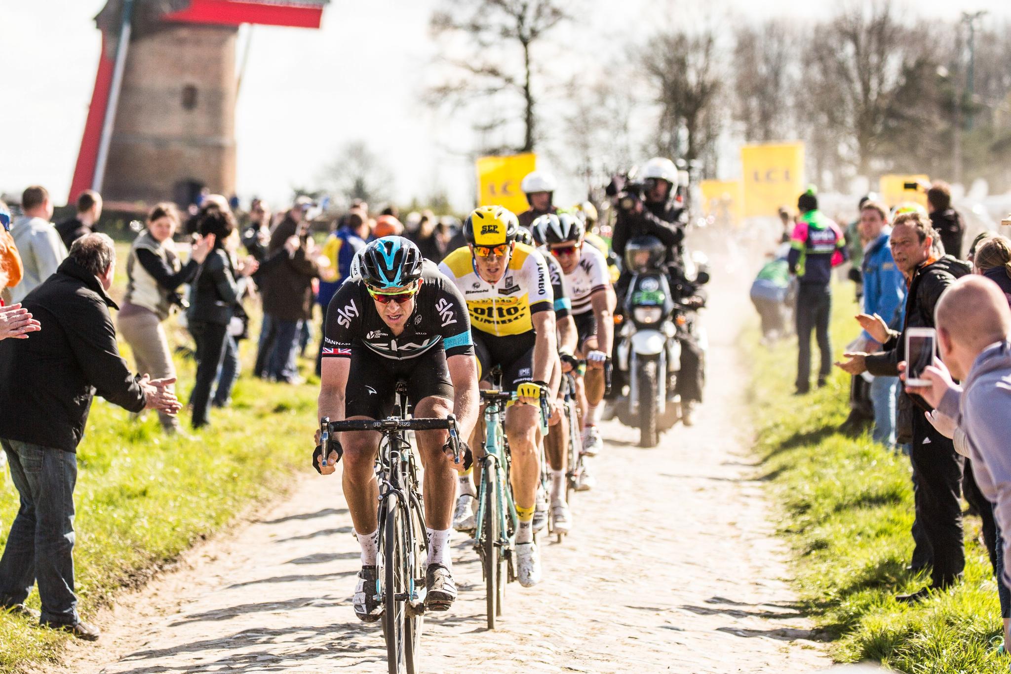 Ian Stannard and Sep Vanmarcke lead a group on a dusty cobbled sector during Paris-Roubaix 2016, with a windmill in the background.