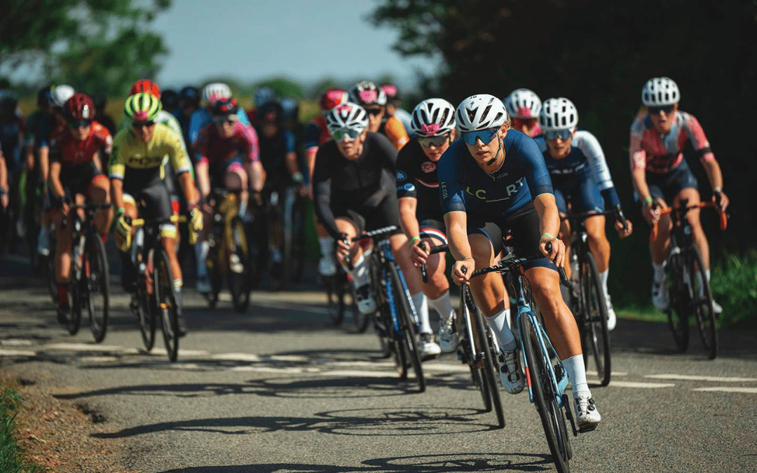 A group of cyclists, including a lead rider in blue and black kit, racing at the UCI Gran Fondo World Championships 2025 on a sunny day.