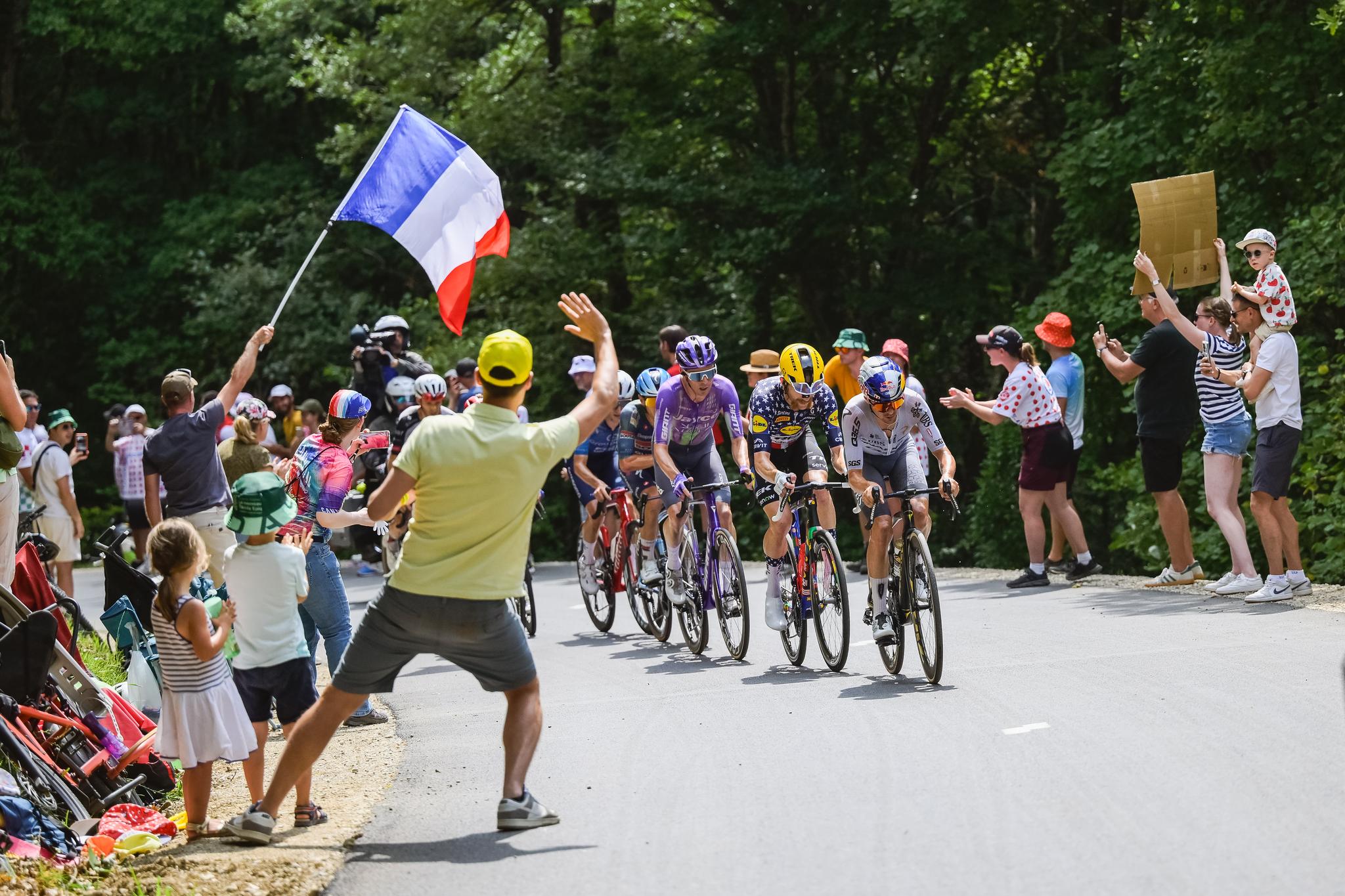 Jonas Vingegaard (Visma-Lease a Bike) and peloton ascend Plateau de Salaison Brison at Tour de France 2026 Stage 15, cheered by a fan waving a French flag.