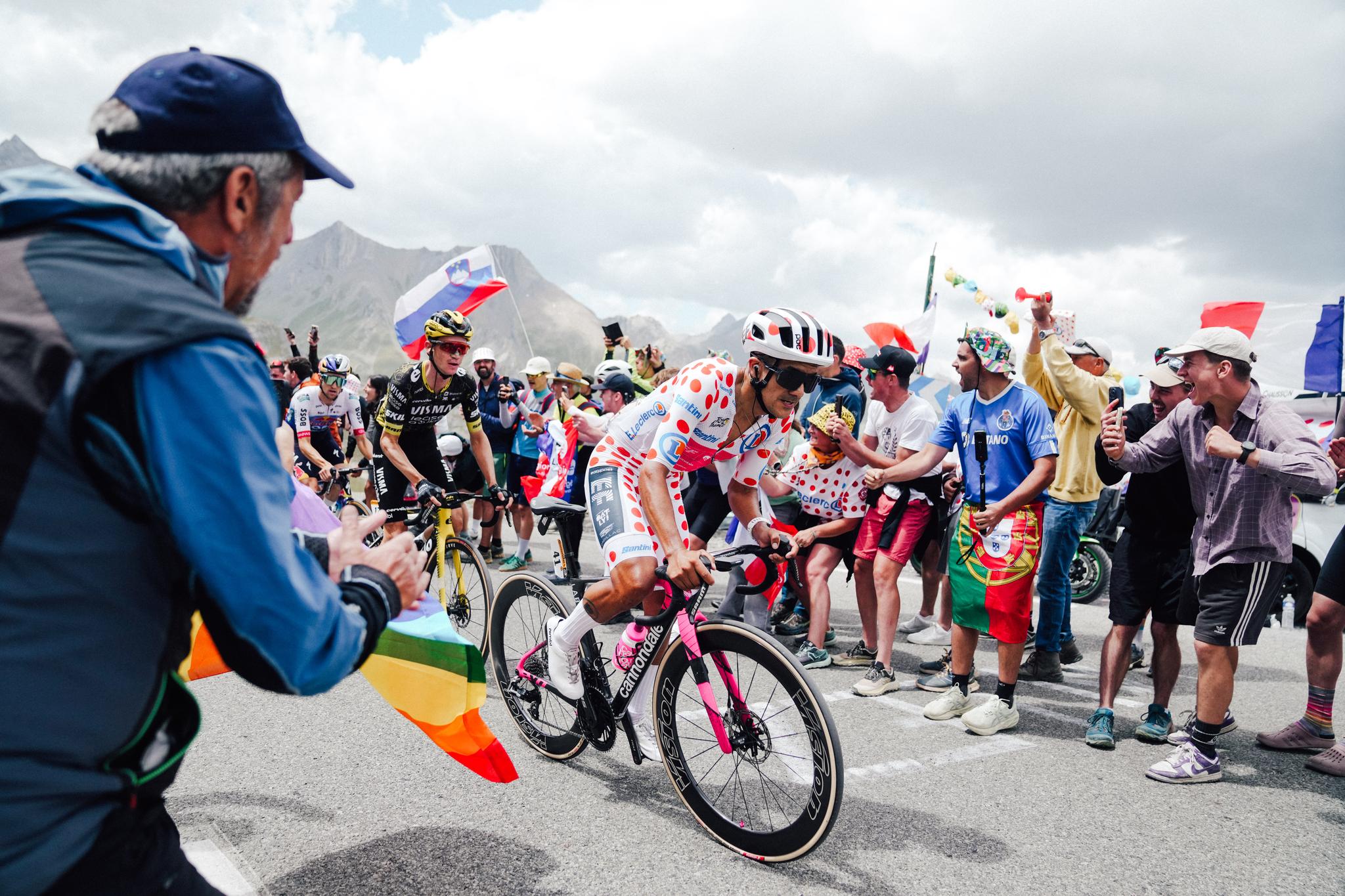 Richard Carapaz in the polka dot jersey climbing Alpe d'Huez at Tour de France 2026, surrounded by cheering fans.