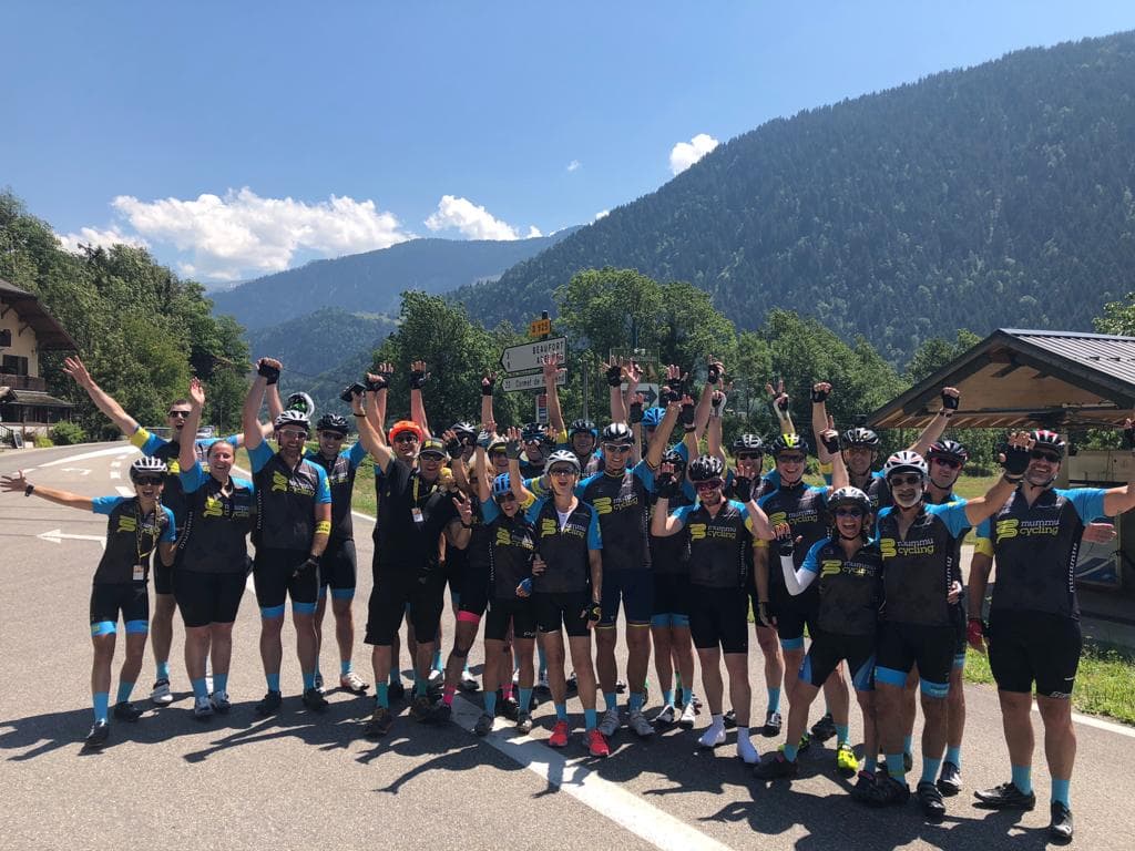Group of cyclists in Mummu Cycling kit celebrating in a mountain landscape.