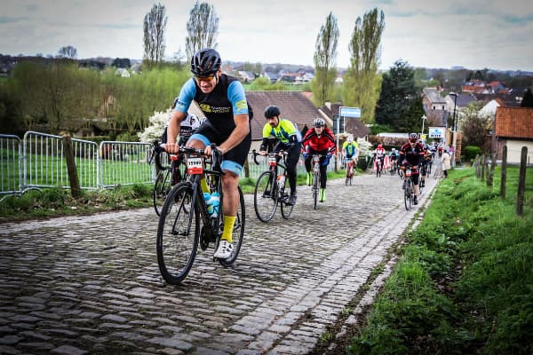 Cyclists climb a steep cobbled road during a 2022 Cobbled Classic, with a rider in a black and blue kit leading a Jumbo-Visma rider.