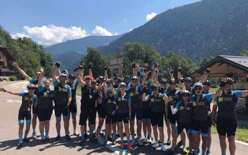 Group of cyclists in Mummu Cycling kit celebrating in a mountain setting.