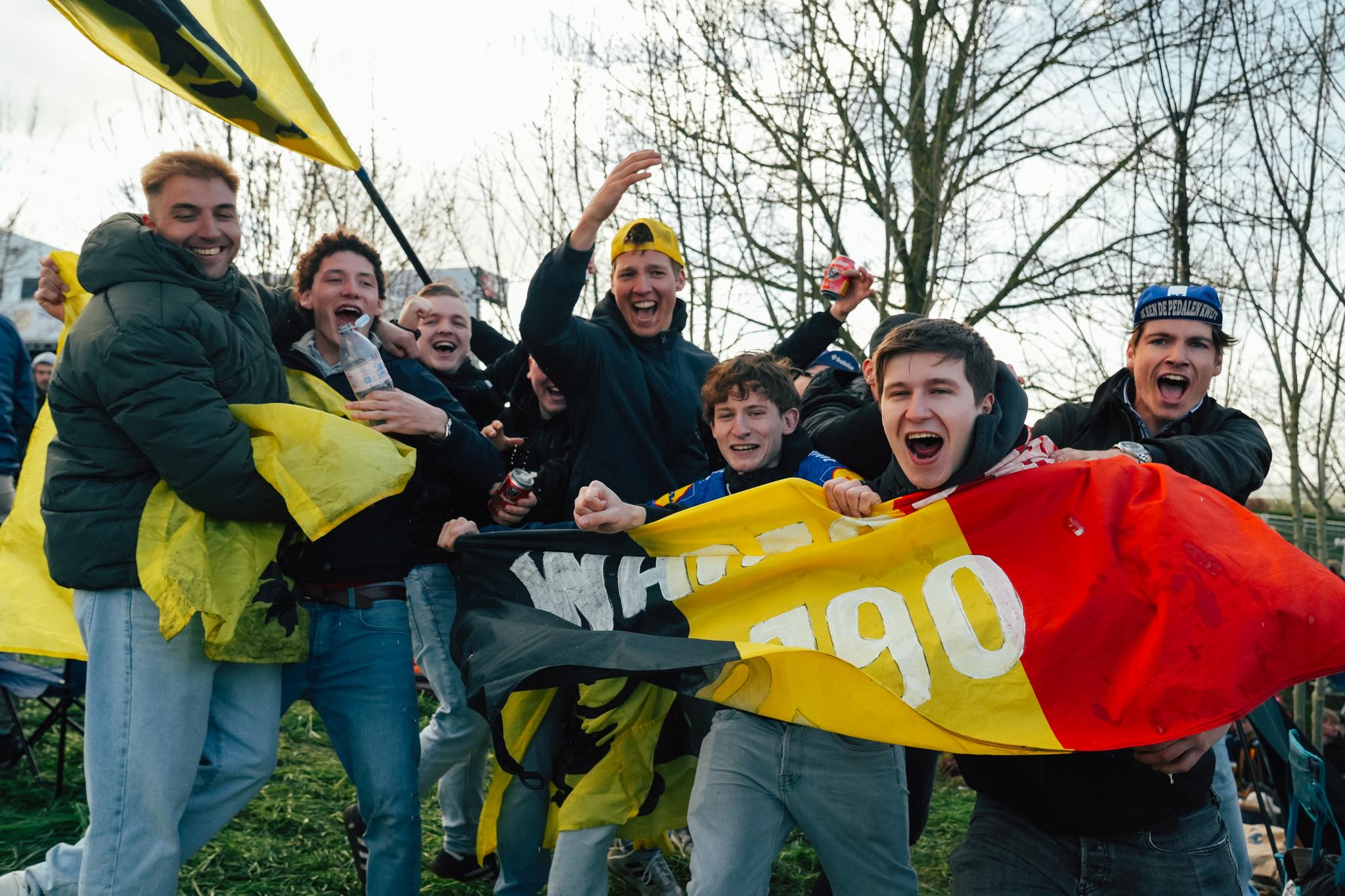 Group of enthusiastic Belgian cycling fans cheering and holding a national flag.