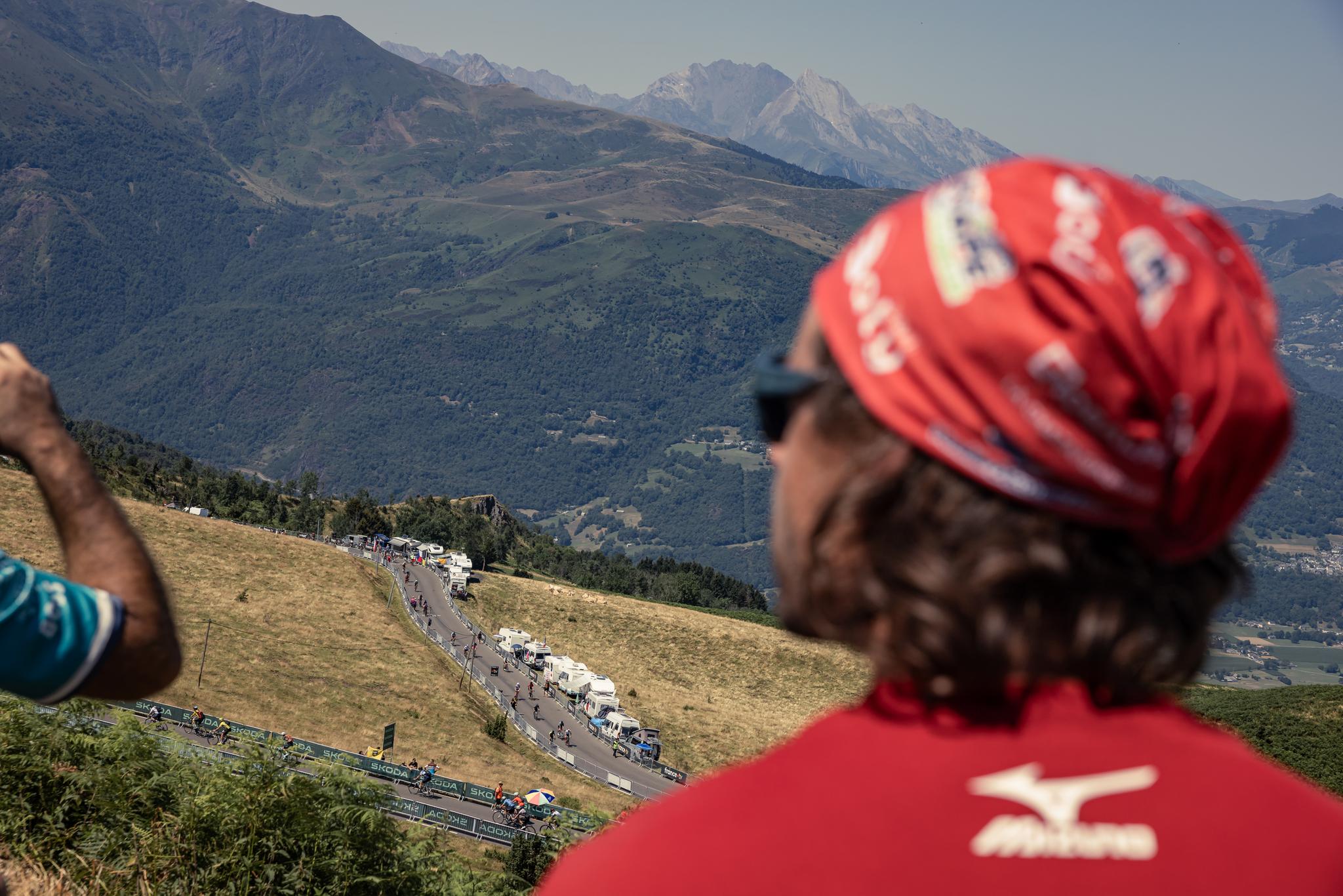 Tour de France Stage 12 peloton climbs a mountain road, spectator in foreground