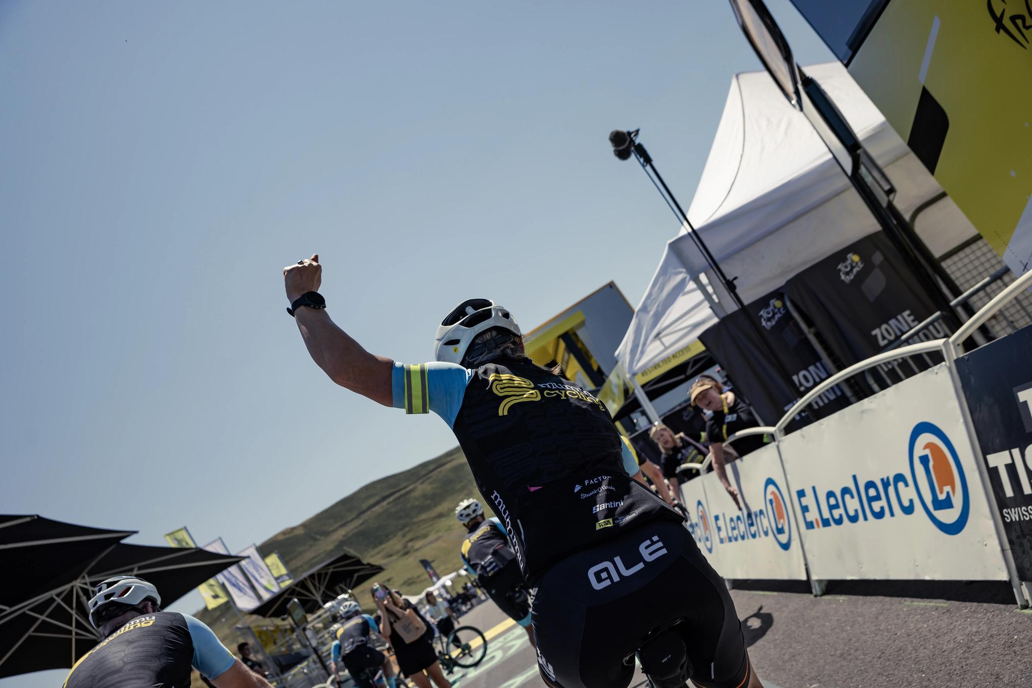 A Mummu Cycling guest raises a celebratory fist while riding across a Tour de France mountain stage finish line.