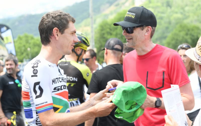 Cyclists in black and blue kits ride past a fan with face paint.