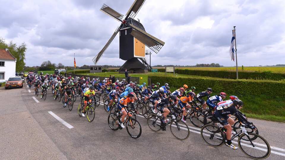 Peloton racing past windmill in flat landscape
