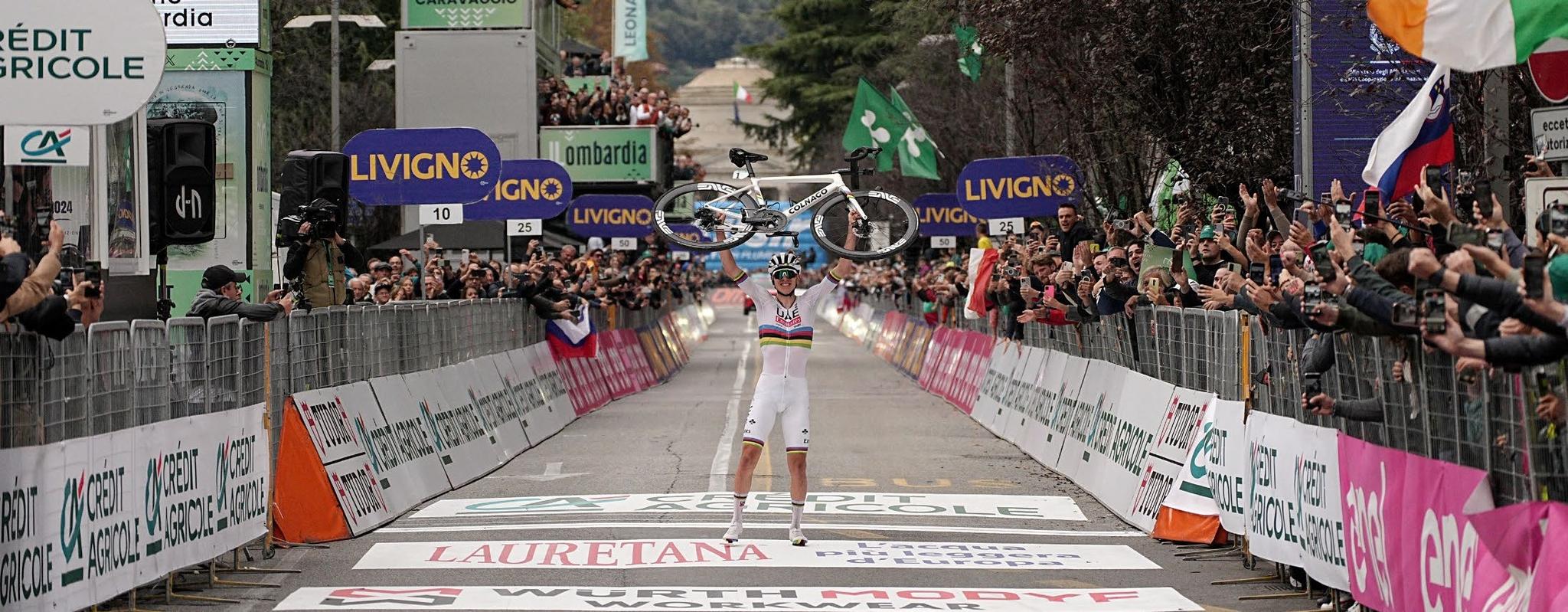 Tadej Pogačar lifts his bike above his head on the finish line of Il Lombardia, crowds either side of the straight