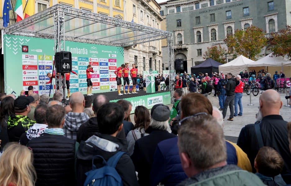 Team presentation on the Il Lombardia start village stage, with the crowd gathered in the piazza