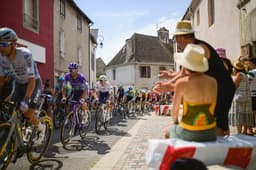 Spectators cheer as the peloton, including the Tour de France King of the Mountains in polka dot jersey, passes through a French town during Stage 12 of the 2026 Tour de France.