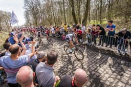 Bora-Hansgrohe rider leading a peloton on a challenging cobbled sector, characteristic of Paris-Roubaix.